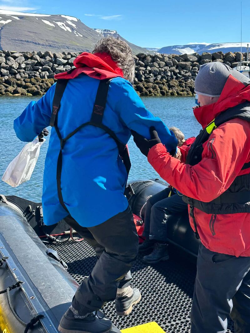 A female traveler uses the Sailor's Grip with an expedition guide as she steps carefully into a Zodiac during an Antarctic expedition cruise.