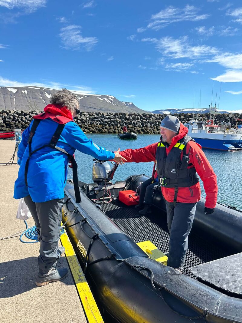 An expedition team member demonstrates the Sailor's Grip while helping a woman safely board a Zodiac from an expedition cruise ship before a shore landing.